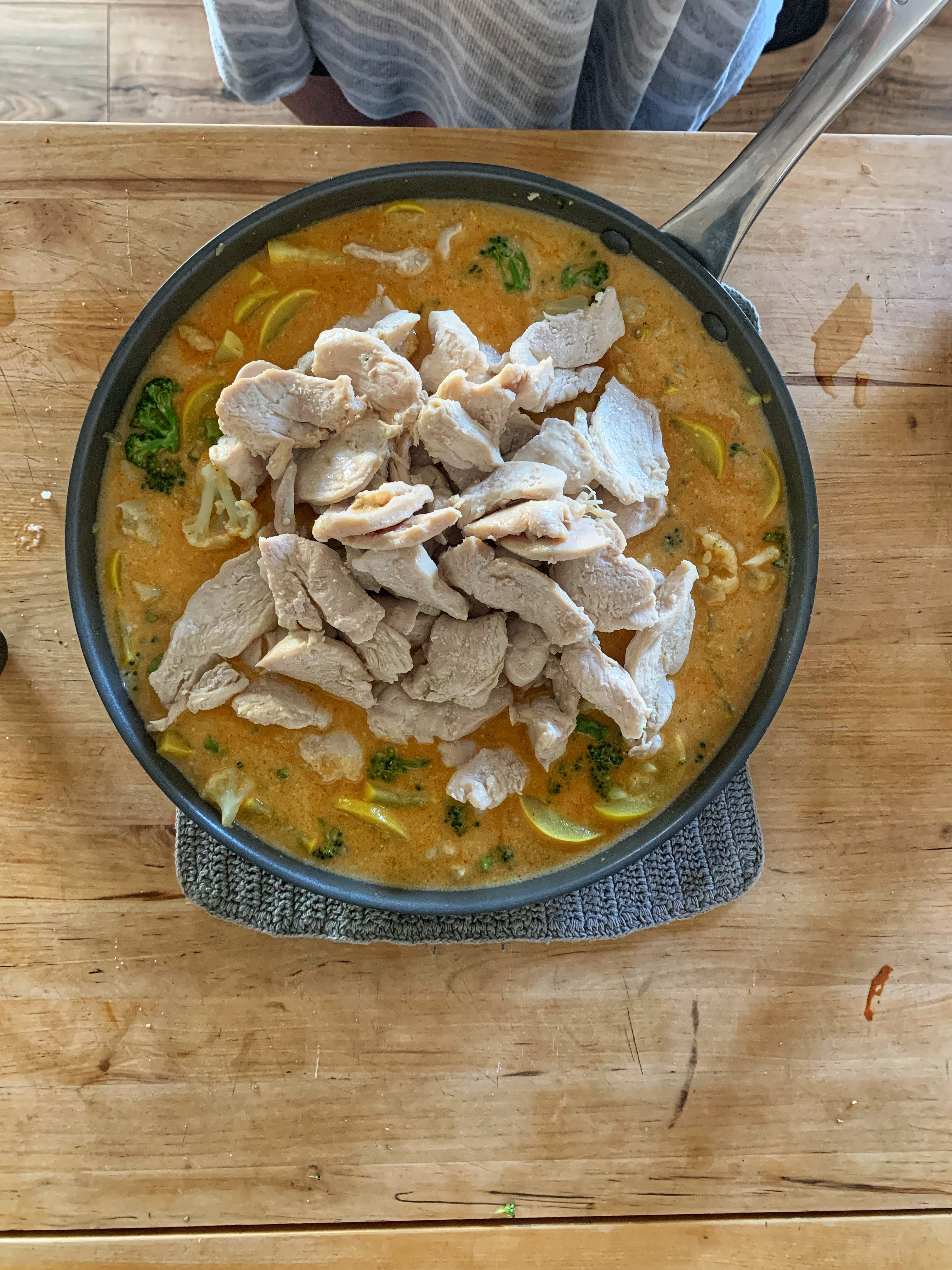 Chicken on top of veggies and curry sauce in skillet