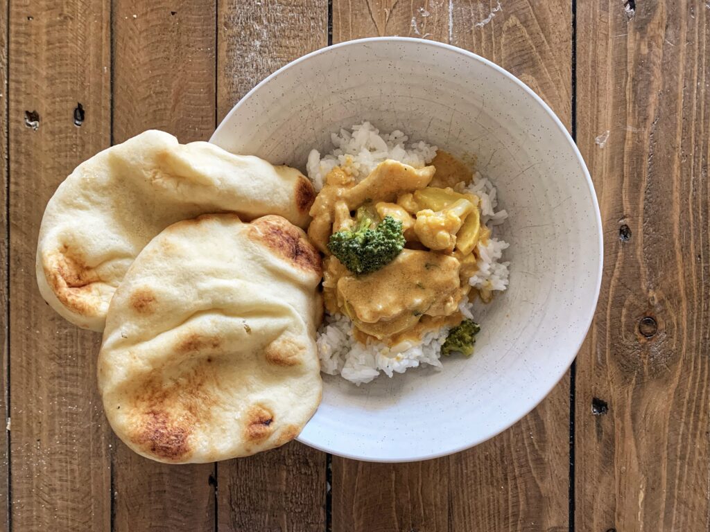 White bowl of Thai Chicken Curry served with naan on a wooden table