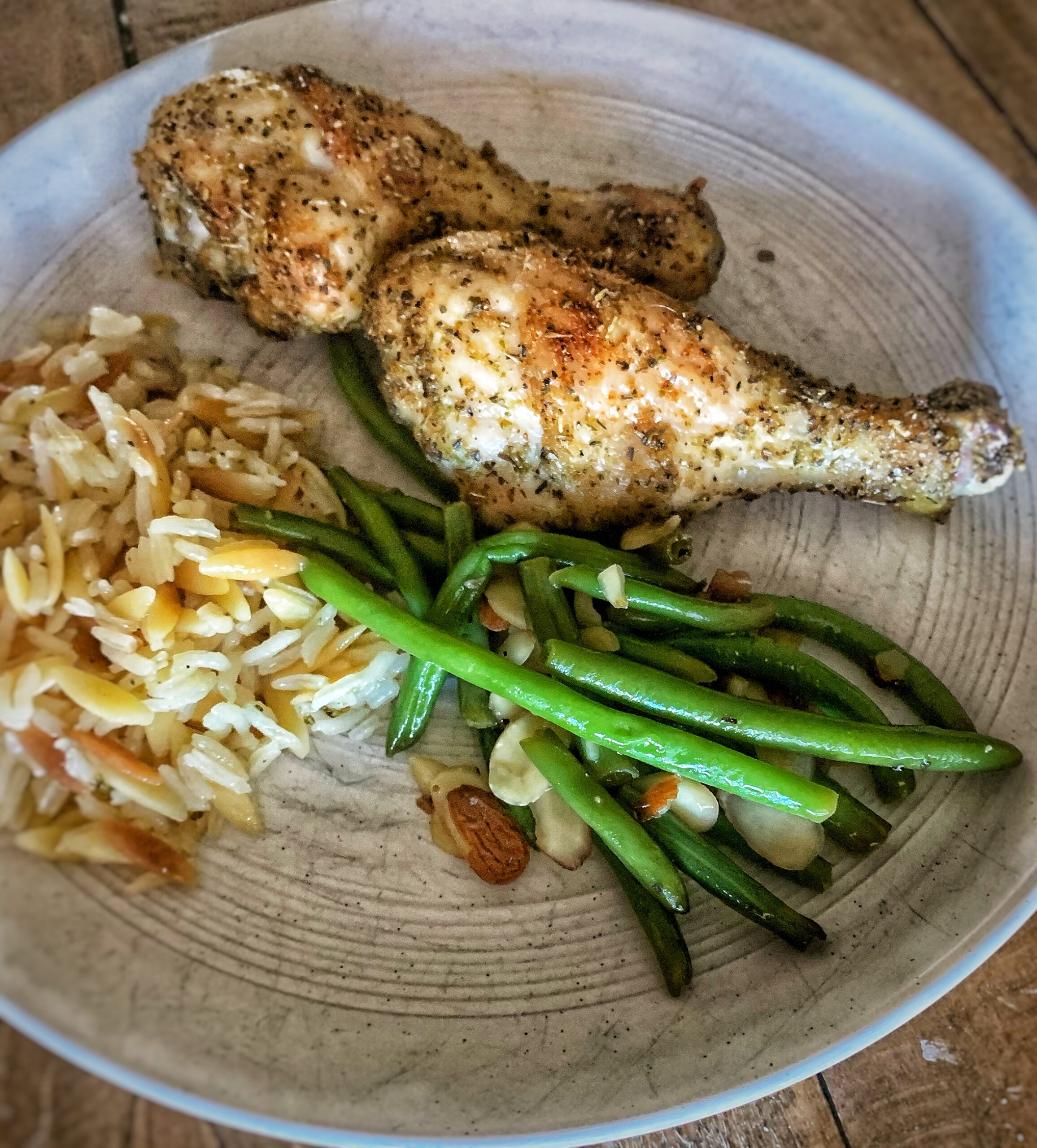 Chicken legs, rice pilaf, and magnolia table green beans amandine on white plate