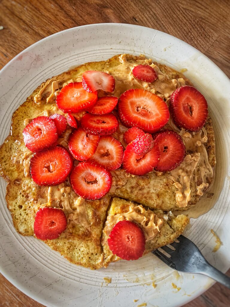 Banana pancake on plate with strawberries, peanut butter, and syrup on top