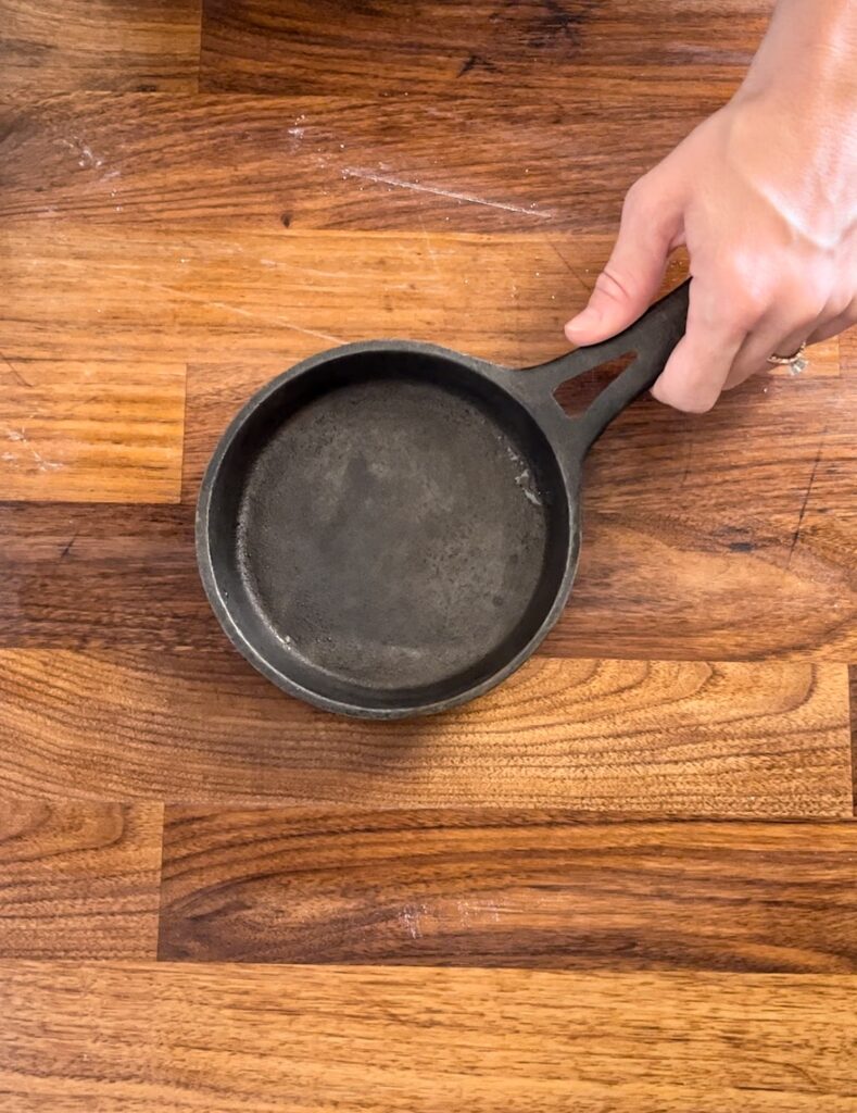 Small cast iron skillet in hand over wooden counter top