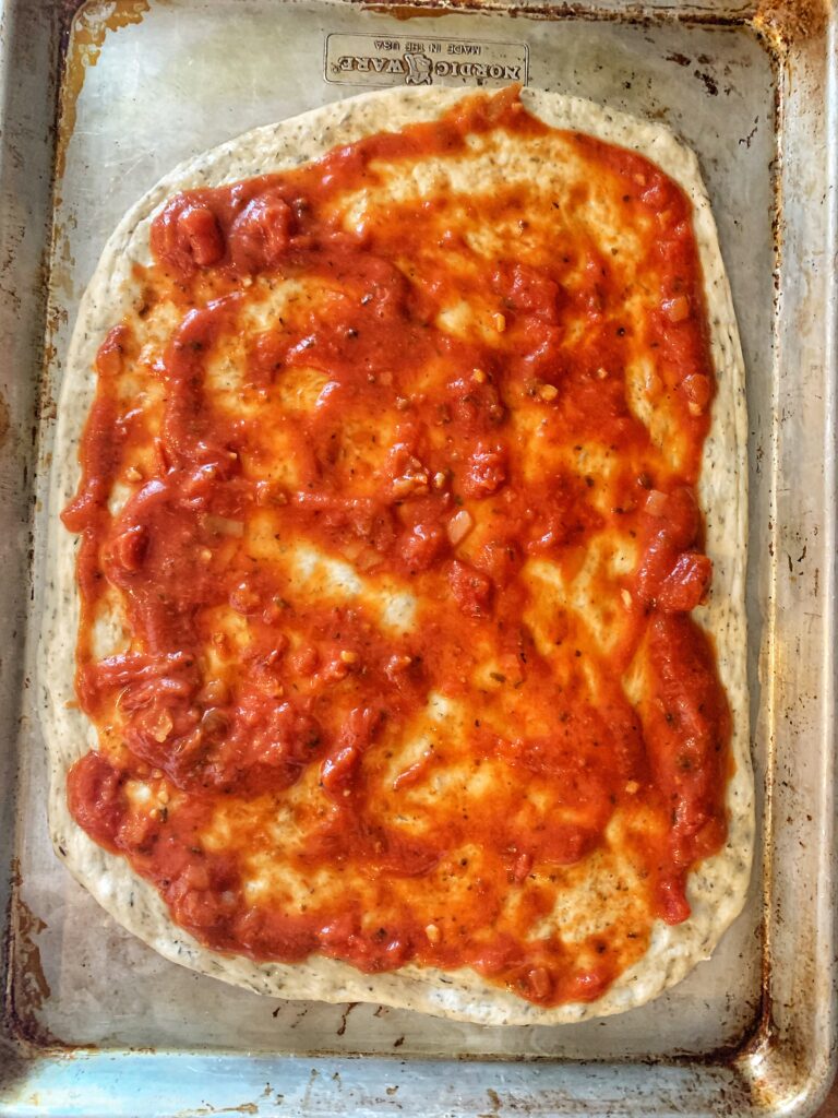 sauce spread on raw pizza dough