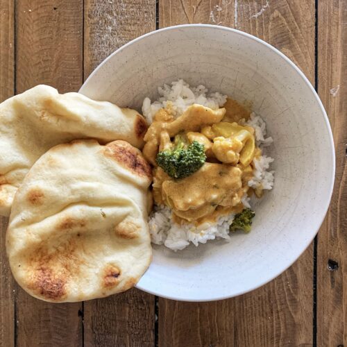 White bowl of Thai Chicken Curry served with naan on a wooden table