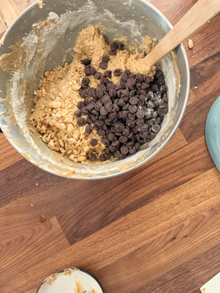 Peanuts and chocolate chips on top of cookie dough in bowl